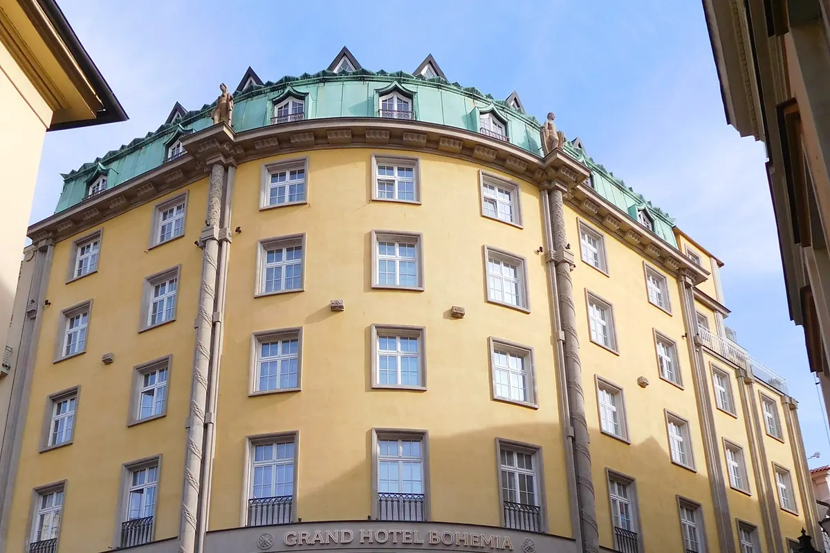 Die geschwungene gelbe Eckfassade des Grand Hotel Bohemia, eines sechsstöckigen Gebäudes mit grünem Dach, in einer Prager Straße.