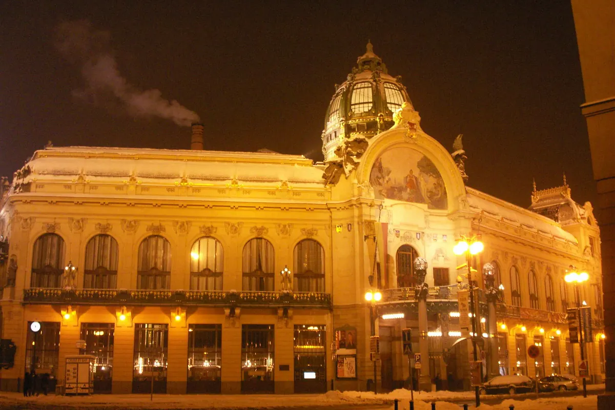 Die Jugendstilfassade des Gemeindehauses in Prag, bei Nacht in goldenes Licht getaucht, mit grüner Kuppel.